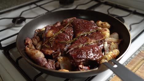 savory beef roast cooked in a skillet with potatoes, onions, and rosemary leaves - pullback shot