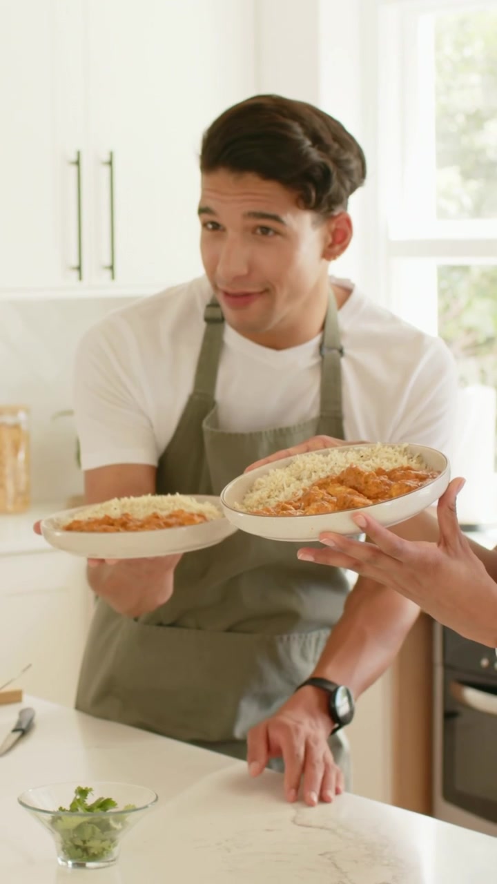Vertical video: Holding man in olive apron offering bowls to guest at home, helper hands entering