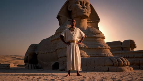 a video still shows a person in ancient attire standing confidently before the sphinx at sunset