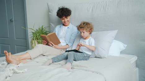 mother and son relaxing in bed, reading and using tablet