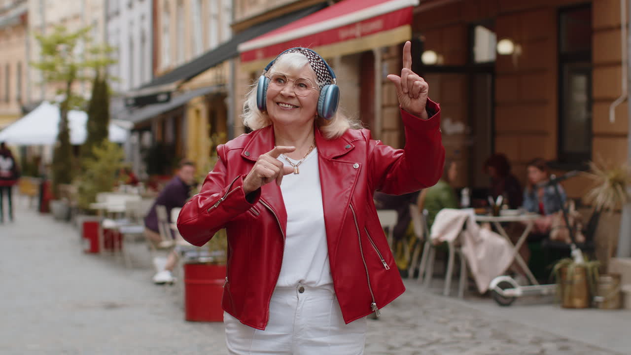Happy senior woman in wireless headphones listening favorite energetic music in urban city street