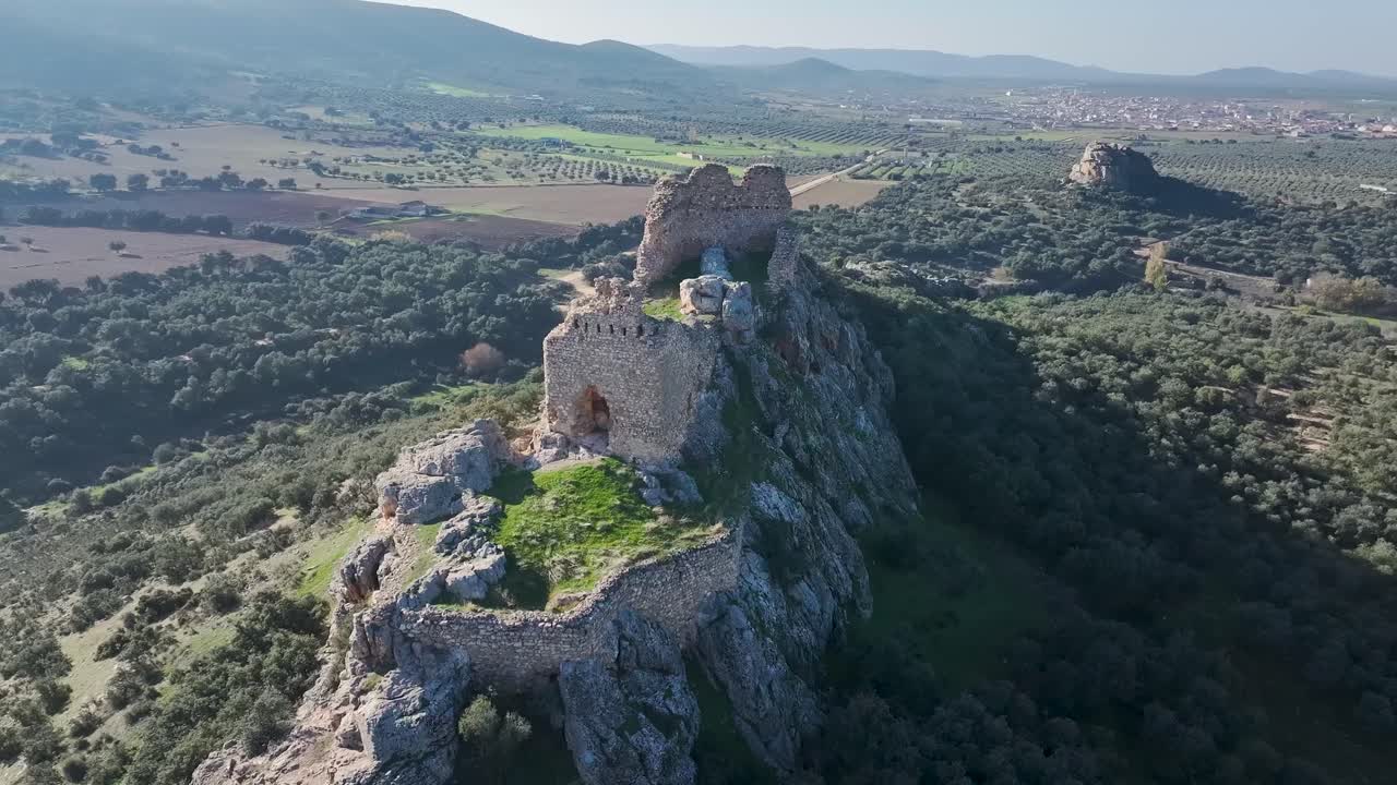 Aerial drone shot of the medieval ruins of Dos Hermanas Castle in Navahermosa, Toledo, Spain. The flight shows the rocky hilltop, remains of the walls, inner entrance, and the town in the distance