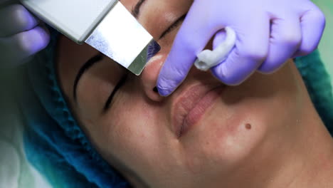 Caucasian woman undergoing skincare procedures. Beauty master uses ultrasonic scrubber for cleansing nose skin pores. Extreme close up.