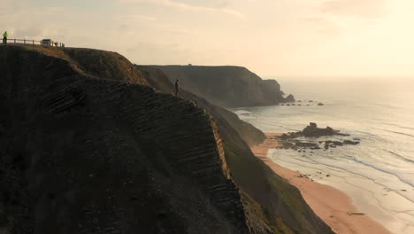 aerial: a man standing on a viewpoint watching the surfers in portugal