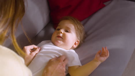 top view of a baby lying on the sofa at home while his mother tickling and playing with him