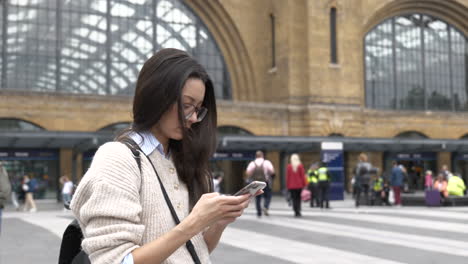 woman stood using her smartphone outside london kings cross station