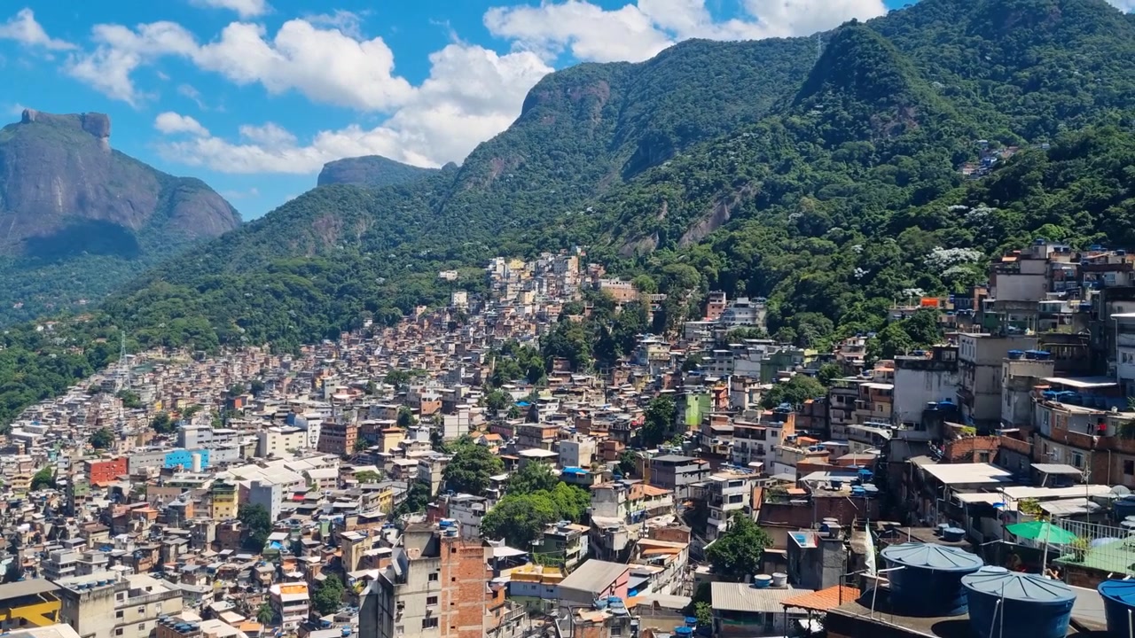 Ampia vista dall'alto sul quartiere Rocinha di Rio de Janeiro, dove dense abitazioni collinari si estendono su un terreno ripido, fondendosi con le montagne verdi circostanti e il drammatico paesaggio urbano, Brasile.