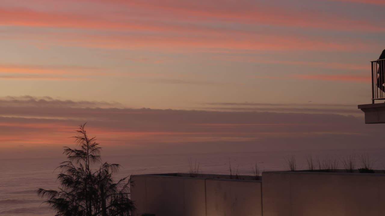 People standing on terras with fence enjoying the beautiful pink sky during sunset.