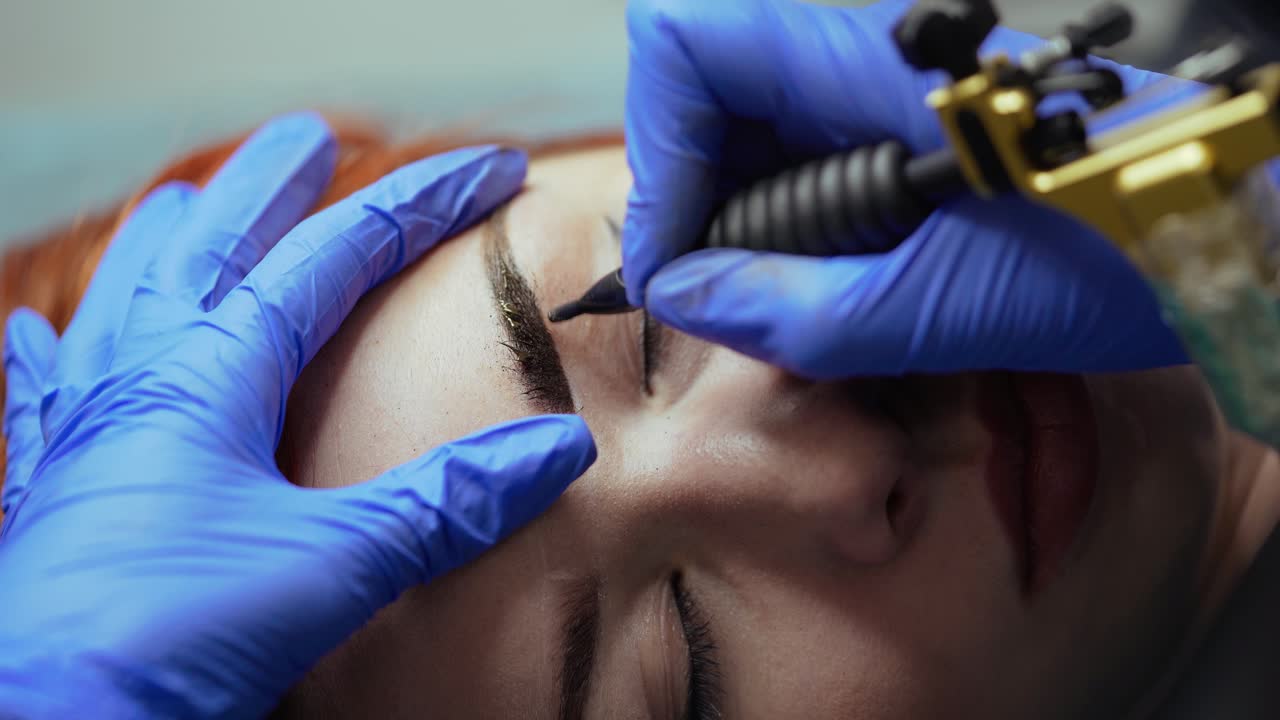 A beauty master is performing tattooing eyebrows in gloves for woman in the cosmetology. Close-up