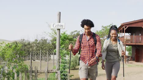 Happy-african-american-couple-with-backpacks,-hiking-with-trekking-poles-together,-slow-motion