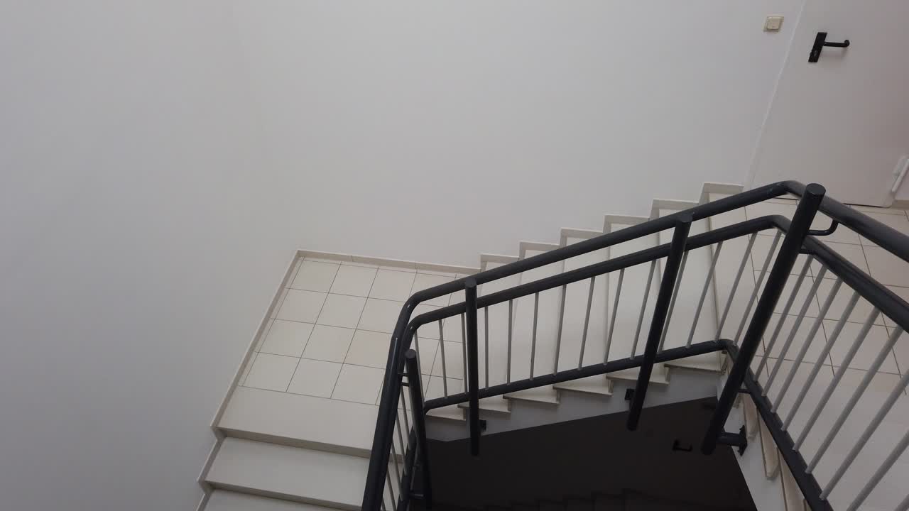 Top to bottom view of a six story stairwell. White walls and white steps, back raining