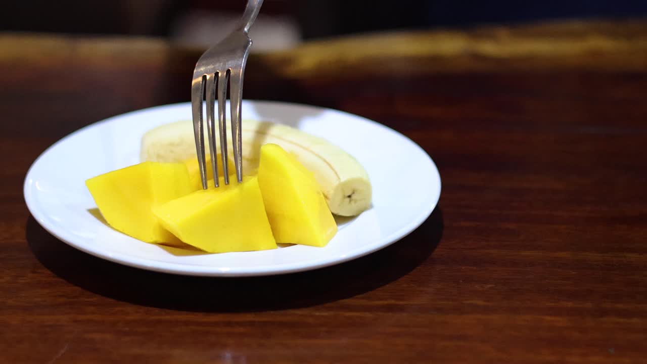 una persona corta y come mango con un tenedor.