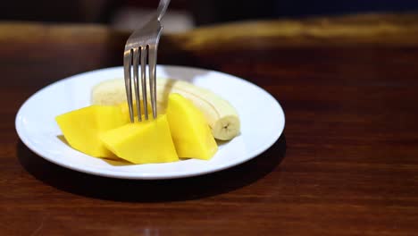 a person slices and eats mango with a fork.