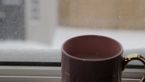 A-hot-beverage-placed-on-a-windowsill-on-a-snowy-day