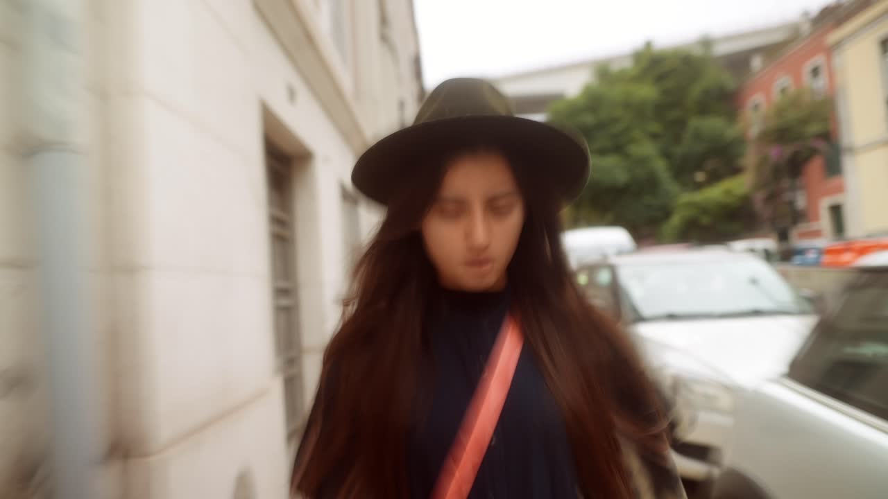 Giovane donna con cappello che cammina disinvolta per una strada urbana