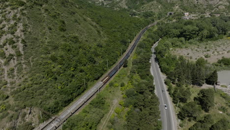 freight train with hopper wagons traveling on the railway in the foothill of mountain in mtskheta, georgia