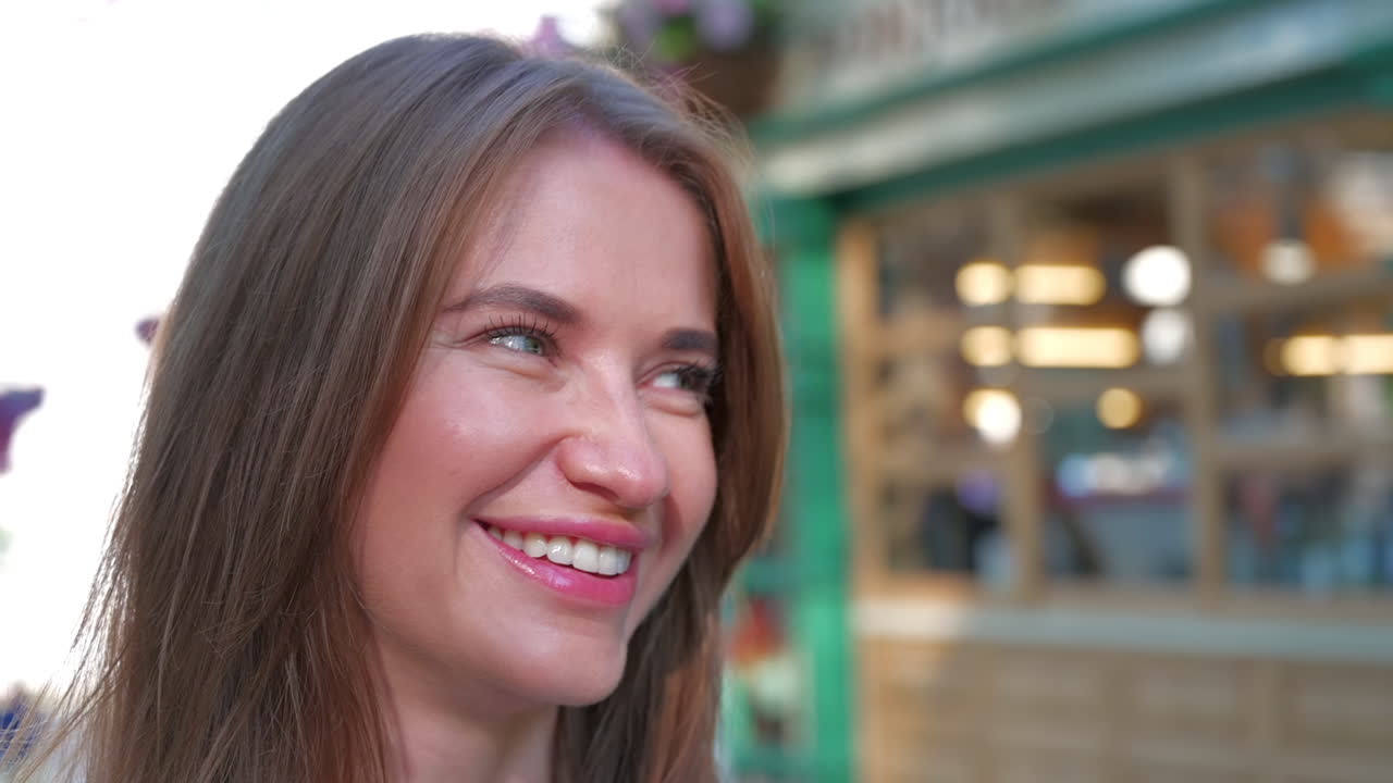 Brunette woman smiling at a table with flowers on it, at an outdoor cafe