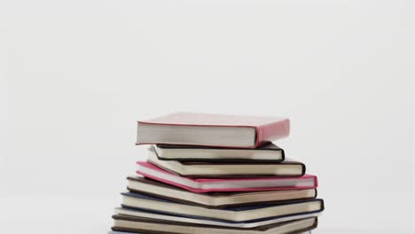 Close-up-of-stack-of-books-on-white-background,-in-slow-motion