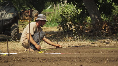 Squatting-farmer-measuring-the-distance-between-rows-in-an-organic-plantation,-sustainable-agriculture-concept