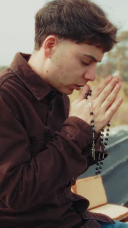 man praying with a rosary and eyes closed on the shore during winter