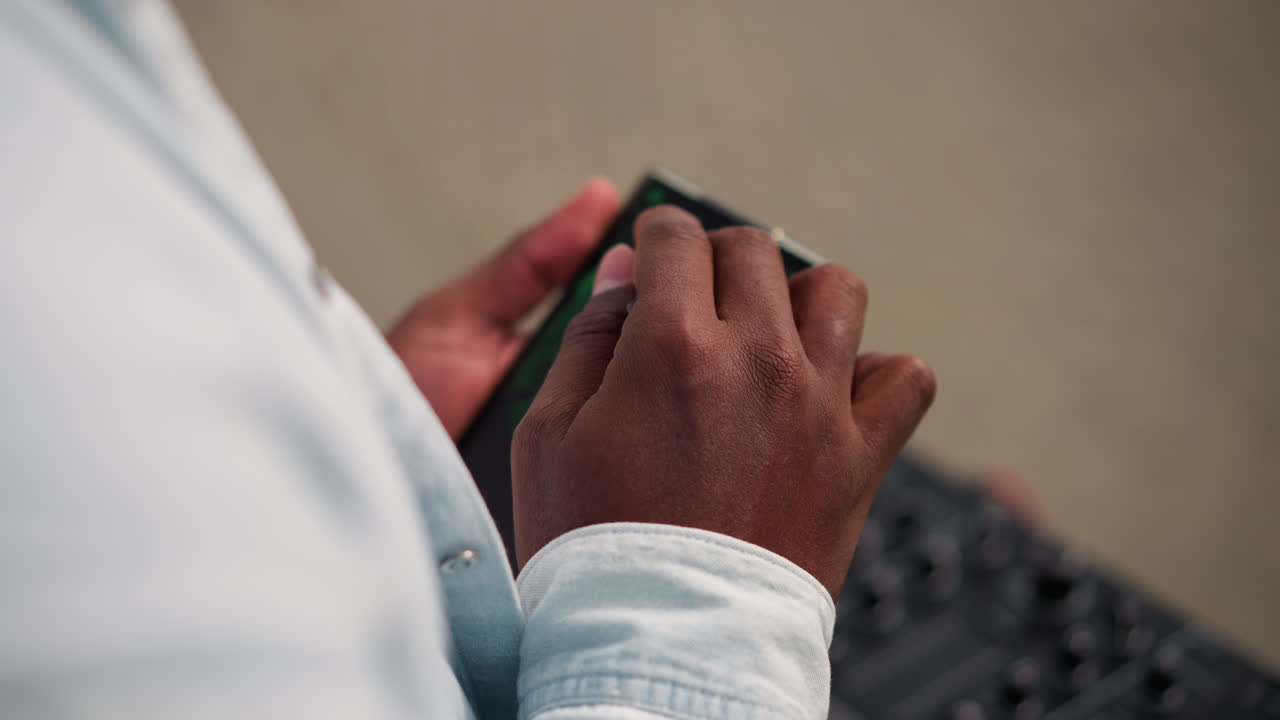 tight shot hands adjusting controller over mixer, behindscenes soundcheck on sidewalk with smartphone track cues, textured fingers tapping pads, moody ambient tones and quiet rehearsal vibe