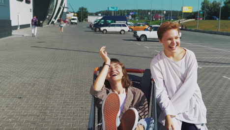 two young women having fun in a shopping cart in a parking lot