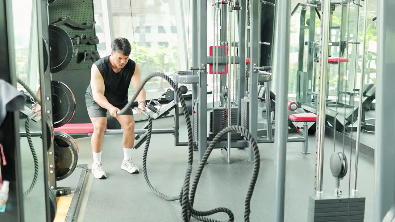 A person performs a vigorous battle rope exercise in a well-lit Bangkok gym, showcasing strength and endurance