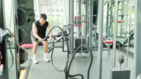 a person performs a vigorous battle rope exercise in a well-lit bangkok gym, showcasing strength and endurance