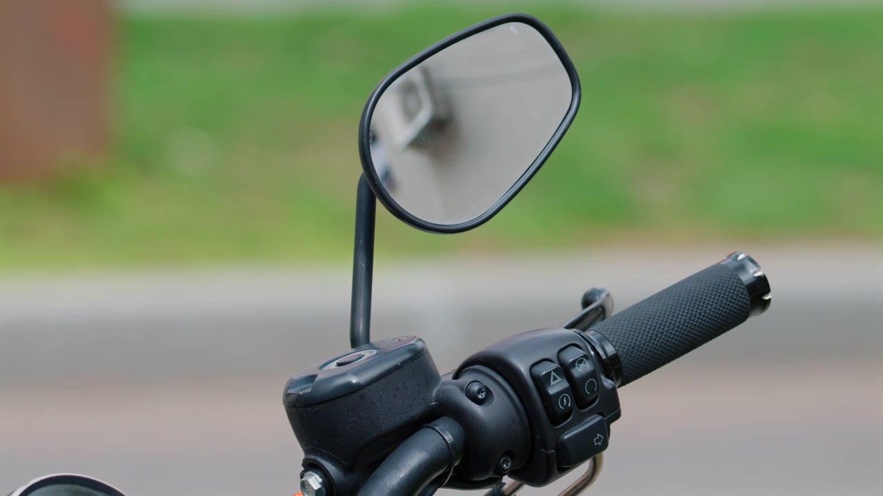 Gros plan détaillé d'un guidon de moto noir, d'un compteur de vitesse, d'un rétroviseur et d'un réservoir de carburant, garée dans une rue urbaine.
