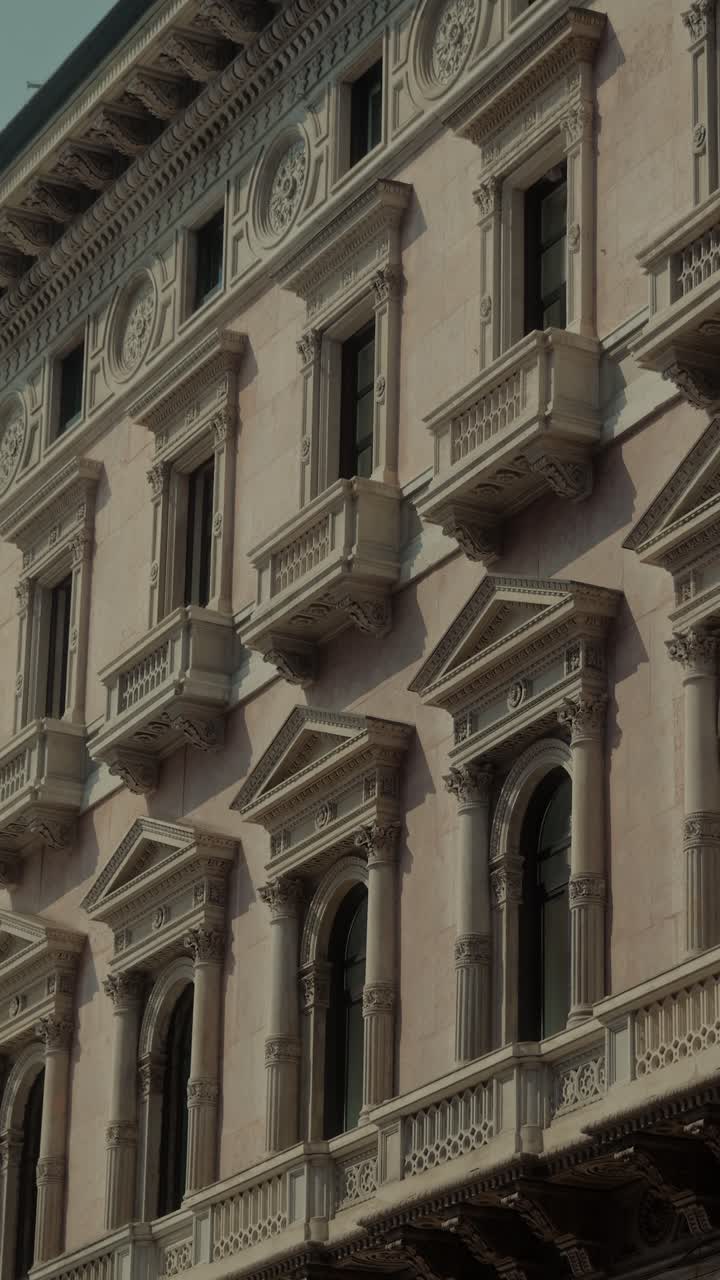 Close-up de janelas e varandas elegantes em uma fachada histórica de Milão, exibindo detalhes arquitetônicos clássicos e charme urbano.