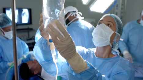 Diverse-surgeons-wearing-surgical-gowns,-applying-drip-in-operating-theatre,-slow-motion