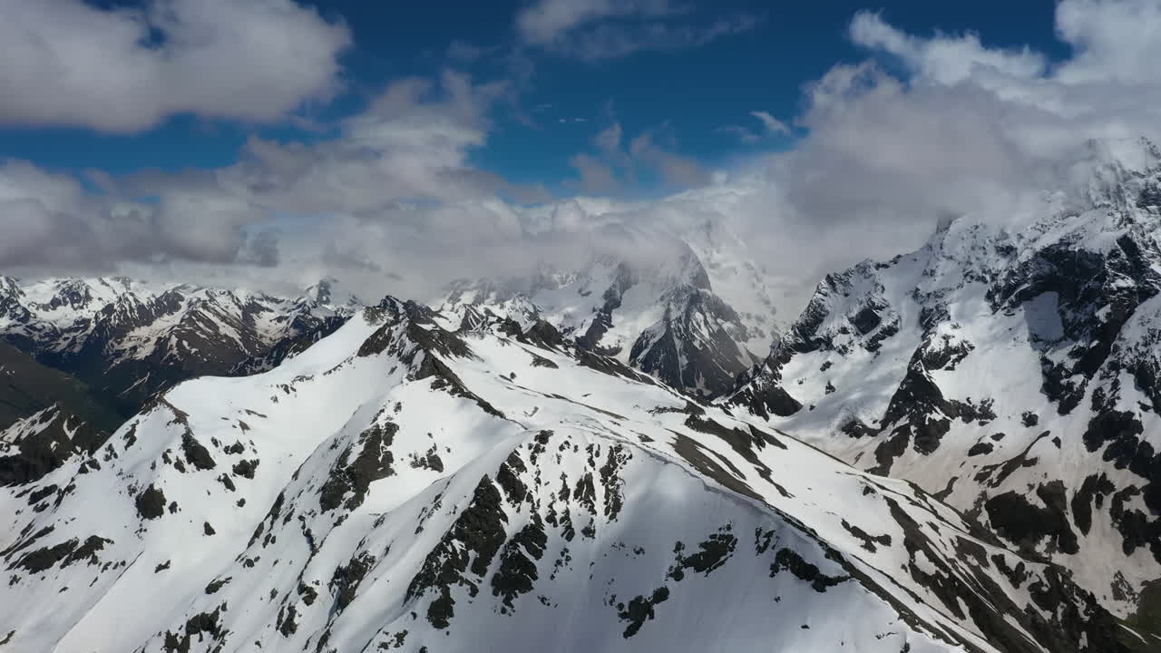 Volo aereo tra le nuvole di montagna sopra splendide vette innevate e ghiacciai.