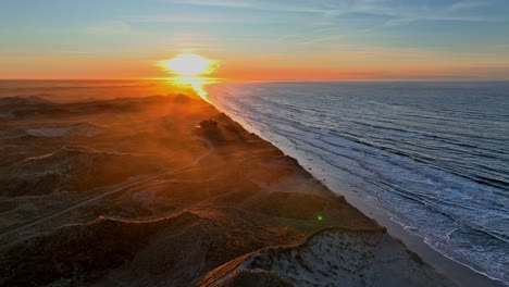 Vista-Panorámica-La-Playa-Está-Bañada-Por-Las-Olas-Del-Mar,-Se-Han-Formado-Altas-Dunas,-La-Casa-De-Verano-Situada-Sobre-Las-Dunas-Está-Rodeada-Por-Una-Niebla-Mística-Y-El-Sol-Se-Pone-En-Una-Tarde-De-Invierno