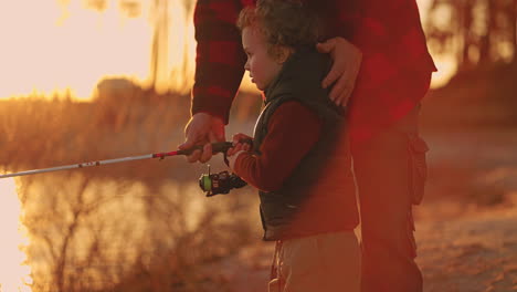 curious little boy is helping father to fish grandfather and grandson are fishing together in sunset