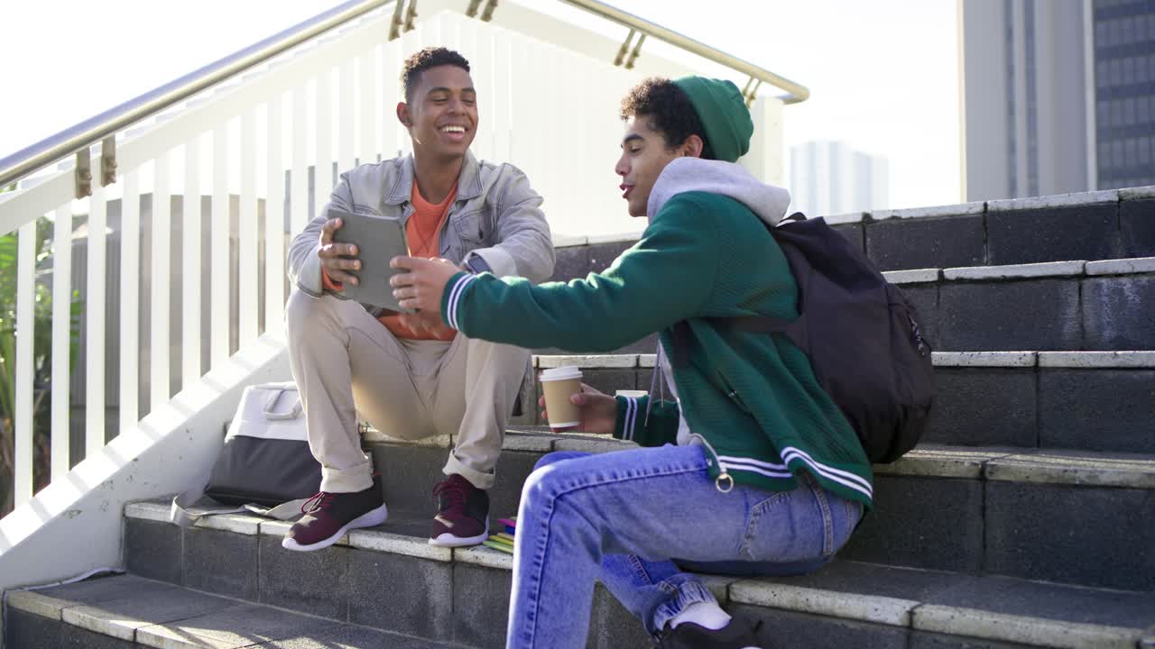 Reacting to gesture, diverse male friends on staircase pulling tablet and laughing at content