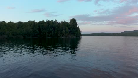 Drone-flying-over-a-lake-following-the-edge-of-the-wood-with-a-nice-sky-in-the-Eastern-Township,-Quebec,-Canada