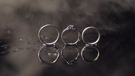 wedding and engagement rings lying on dark water surface shining with light