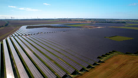 sobrevuelo aéreo moderna granja solar y parque de turbinas eólicas en segundo plano el día de verano