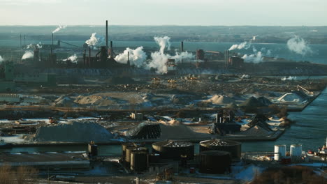 Industrial-complex-by-the-water-with-smokestacks-and-steam-during-daylight,-wide-shot