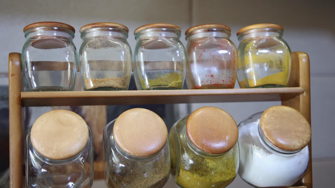 Organized kitchen spices in clear glass jars on a wooden rack, vibrant culinary ingredients ready for cooking