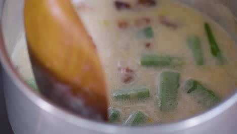 Close-up-shot-stir-with-wooden-spoon-a-pot-of-cream-stew-with-bacon-and-okra