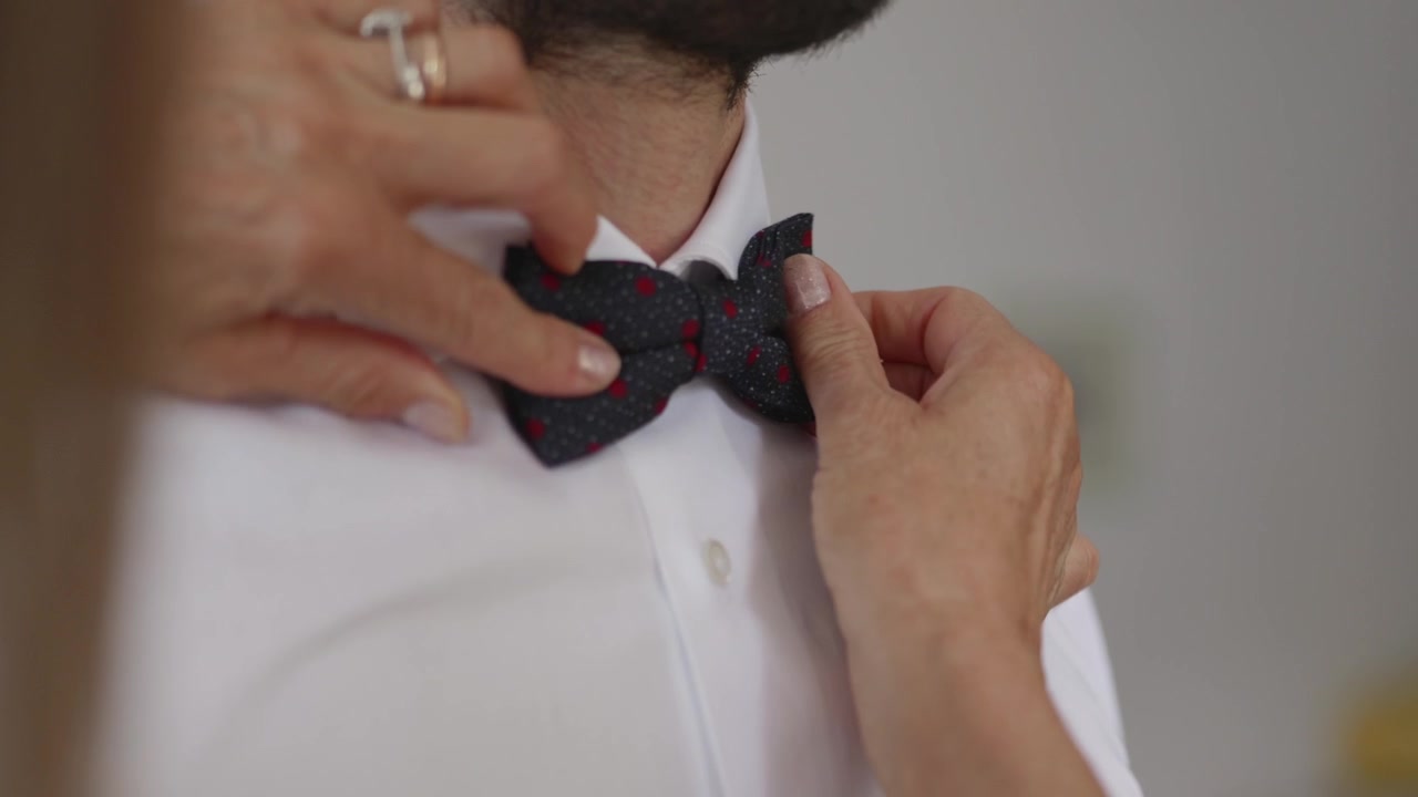 Madre che sistema il papillon dello sposo durante i preparativi del matrimonio. Momento familiare emozionante prima della cerimonia, che evidenzia cura, eleganza e attesa.