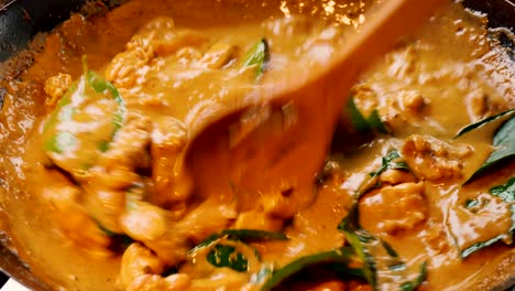 deliciosa comida tailandesa de pollo y verduras y curry rojo se cocinan y se revuelven en un wok negro con una cuchara de madera enrejada, cierre estático