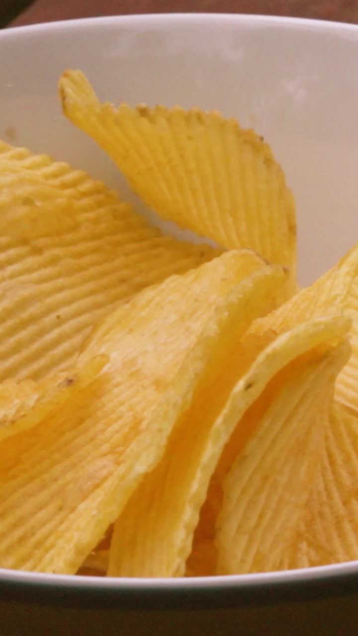 Crinkle cut potato chips falling into white bowl in slow motion. Unhealthy eating food close-up. Perfect for food documentaries. Vertical video 9:16 format. Ideal for social media reels