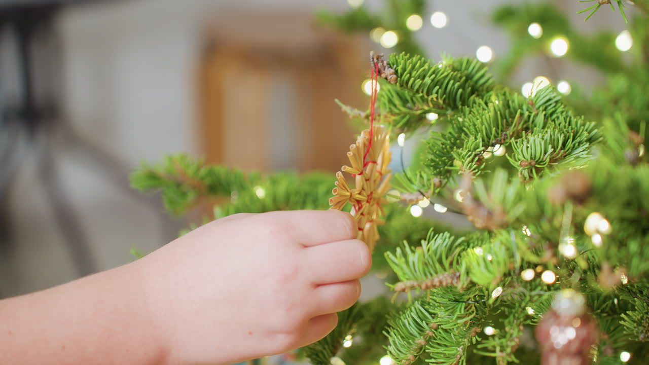 Close view of hand touching natural ornament hanging on christmas tree with blurred background, glowing lights, festive atmosphere, cozy indoor decoration during joyful winter holiday season