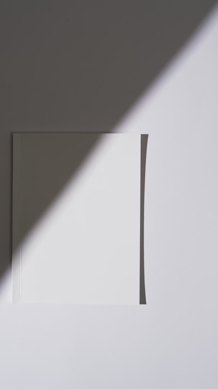 Vertical video of shadow over book with blank pages and copy space on white background