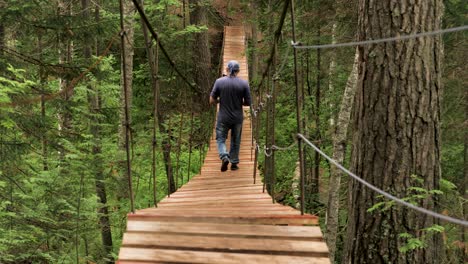 man walking across a wooden suspension bridge in the woods