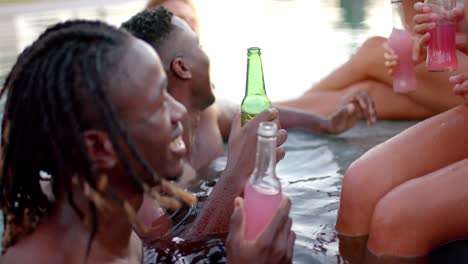 amigos diversos felices con bebidas animando en la piscina en cámara lenta