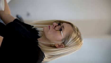 blonde haired female office worker wearing glasses glancing at screens in office