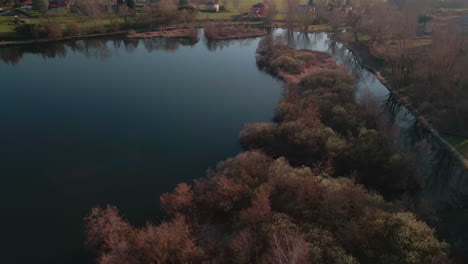 calm water lake surrounded by the nature of the italian countryside during sunset in lago di annone, italy - aerial drone shot